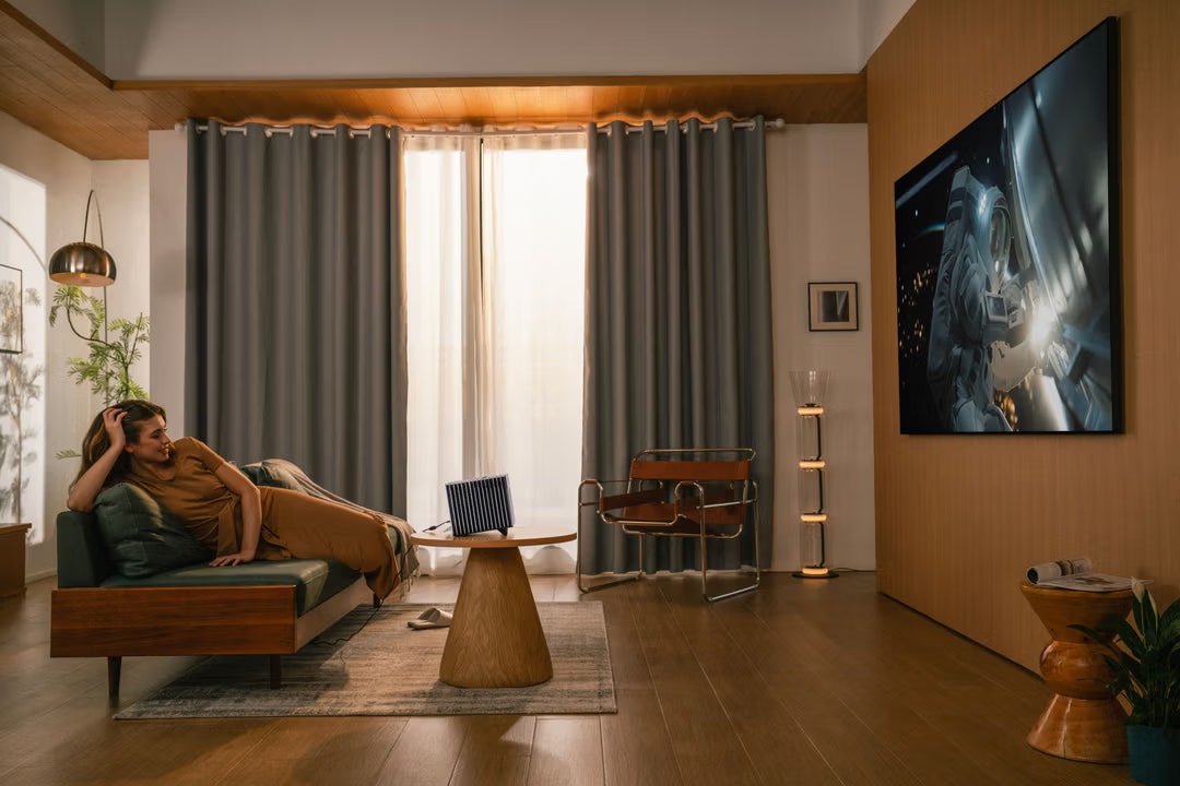 Entspannte Frau liegt auf Sofa in gemütlichem Wohnzimmer und schaut entspannt auf großes projiziertes Bild an der Wand – augenschonendes Heimkino mit Beamer statt direktem Bildschirm.